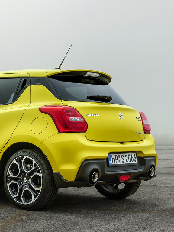 Von hinten fotografierter Suzuki Swift Sport Hybrid in Champion Yellow, Fokus auf der Heckpartie.