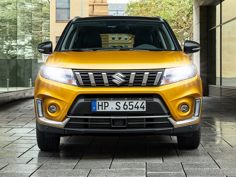 Frontansicht eines Suzuki Vitara Hybrid in Solar Yellow Pearl Metallic mit eingeschaltetem Licht.