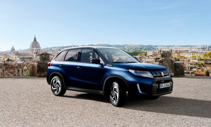 Leicht seitliche Aufnahme eines Suzuki Vitara Hybrid in Blue Sphere Pearl Metallic über den Dächern einer italienischen Stadt.